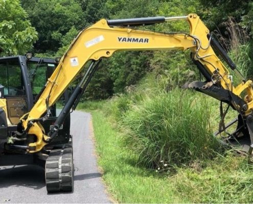 A machine with an arm that is trimming grass on the side of the road.