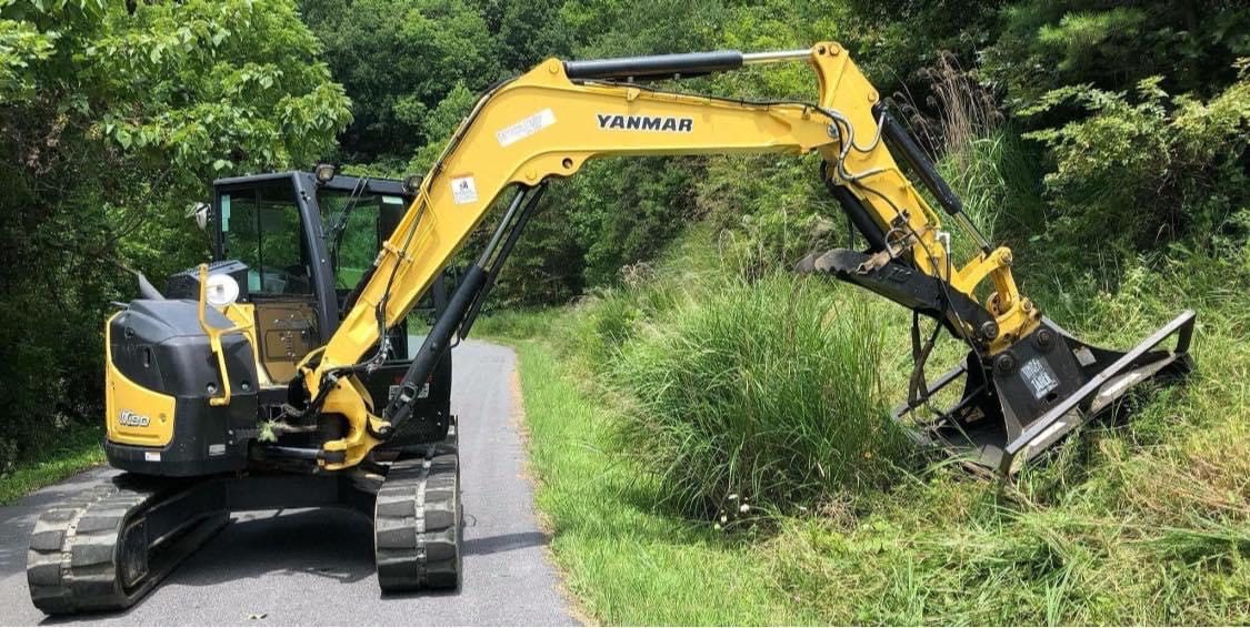 A machine with an arm that is trimming grass on the side of the road.