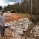 A man stands near a creek where large rocks line the stream to prevent erosion.